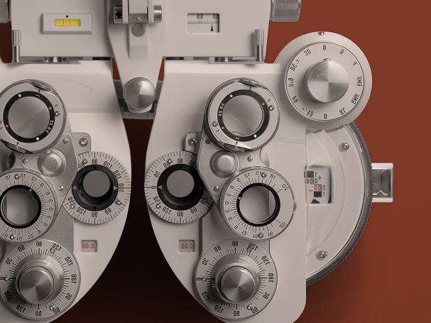 Close-up of a phoropter used for eye exams, showing detailed dials and lenses against a warm terracotta background.